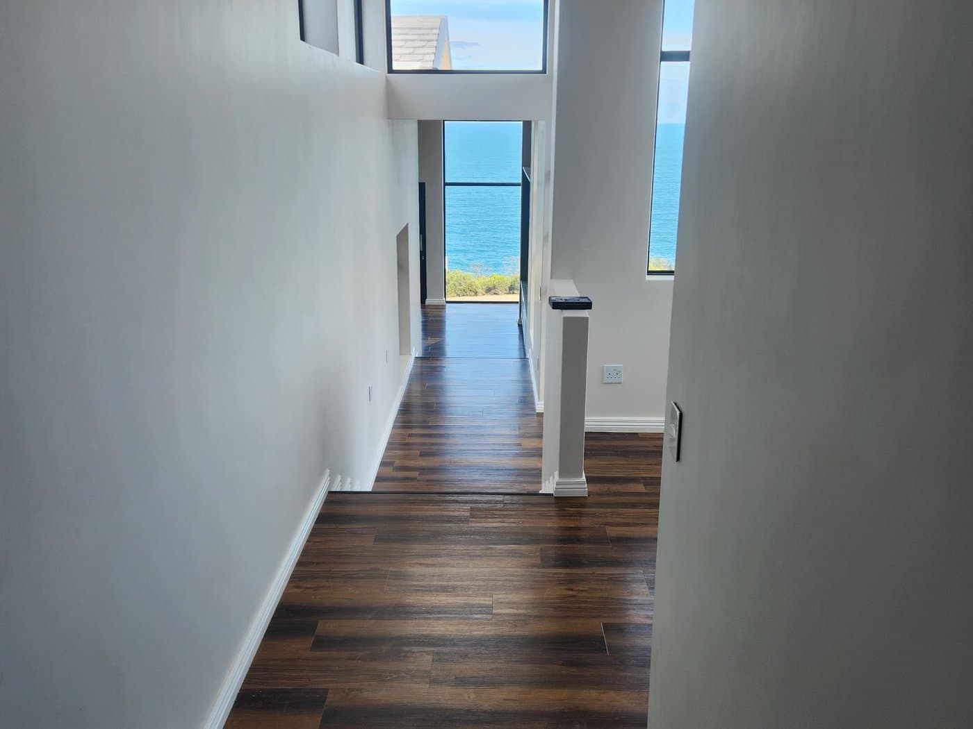 A hallway with dark timber floors opening onto a full height window over the sea