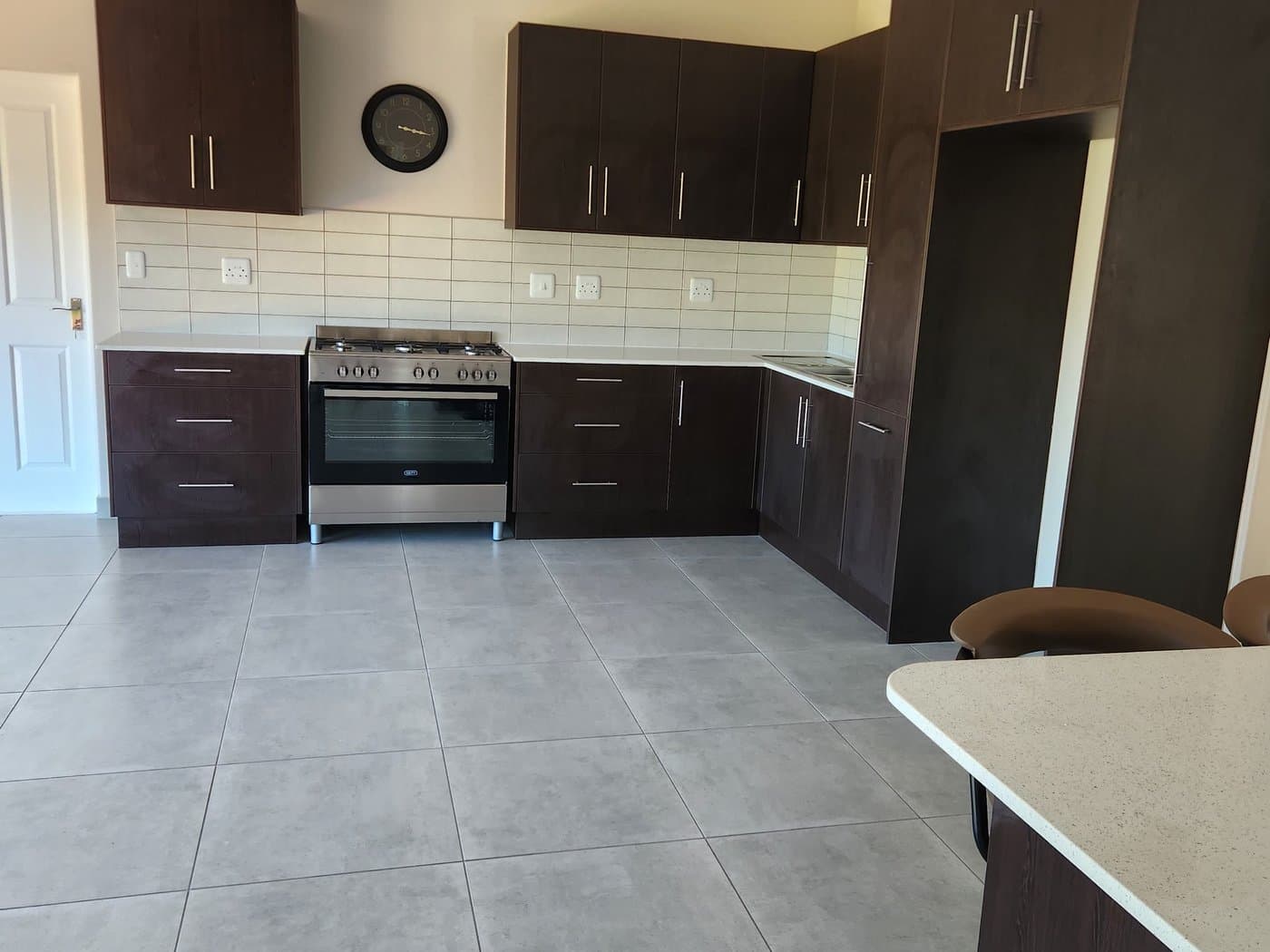 A fitted kitchen with dark cabinetry, tiled floors and a wall clock