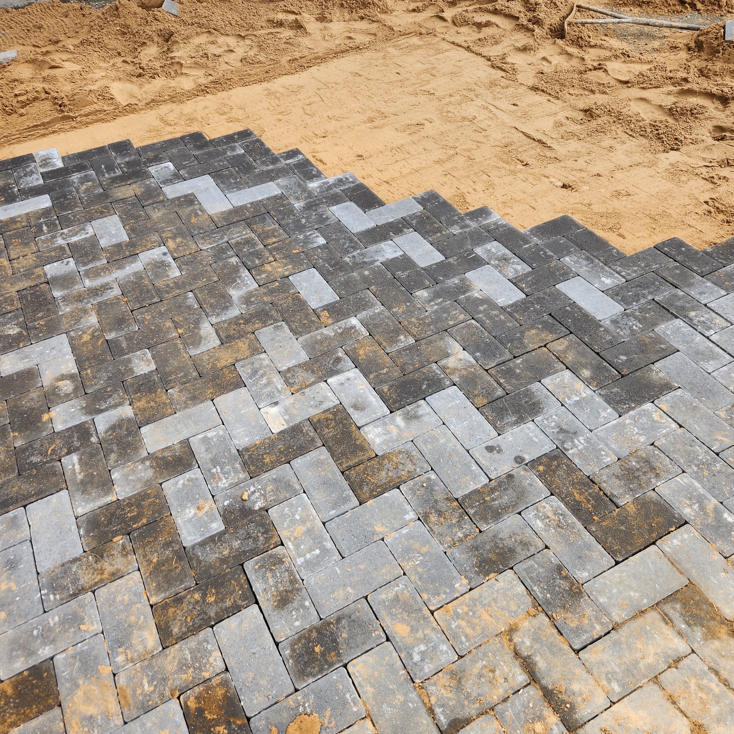 Grey cobbled pavers being laid by hand on a prepared bed