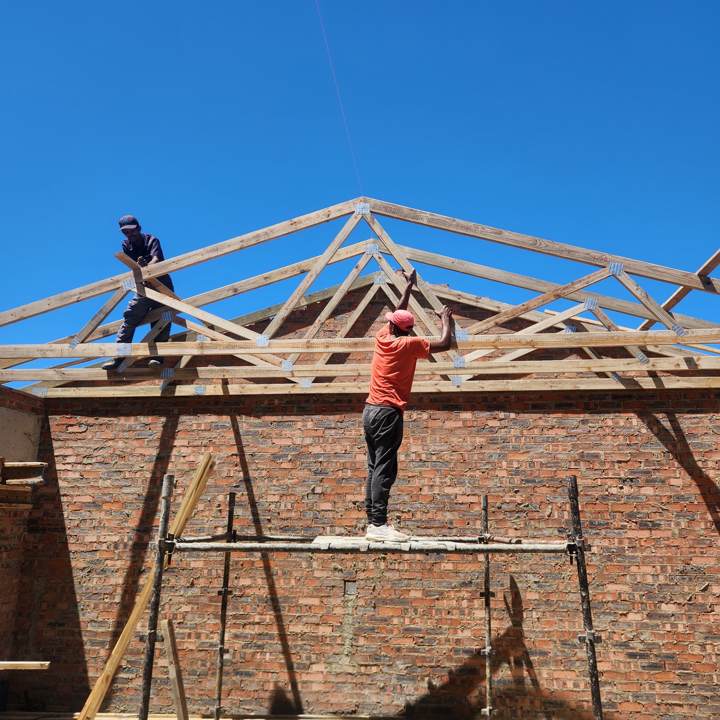 Two of the A-Tech team setting roof trusses on a new build against a clear sky