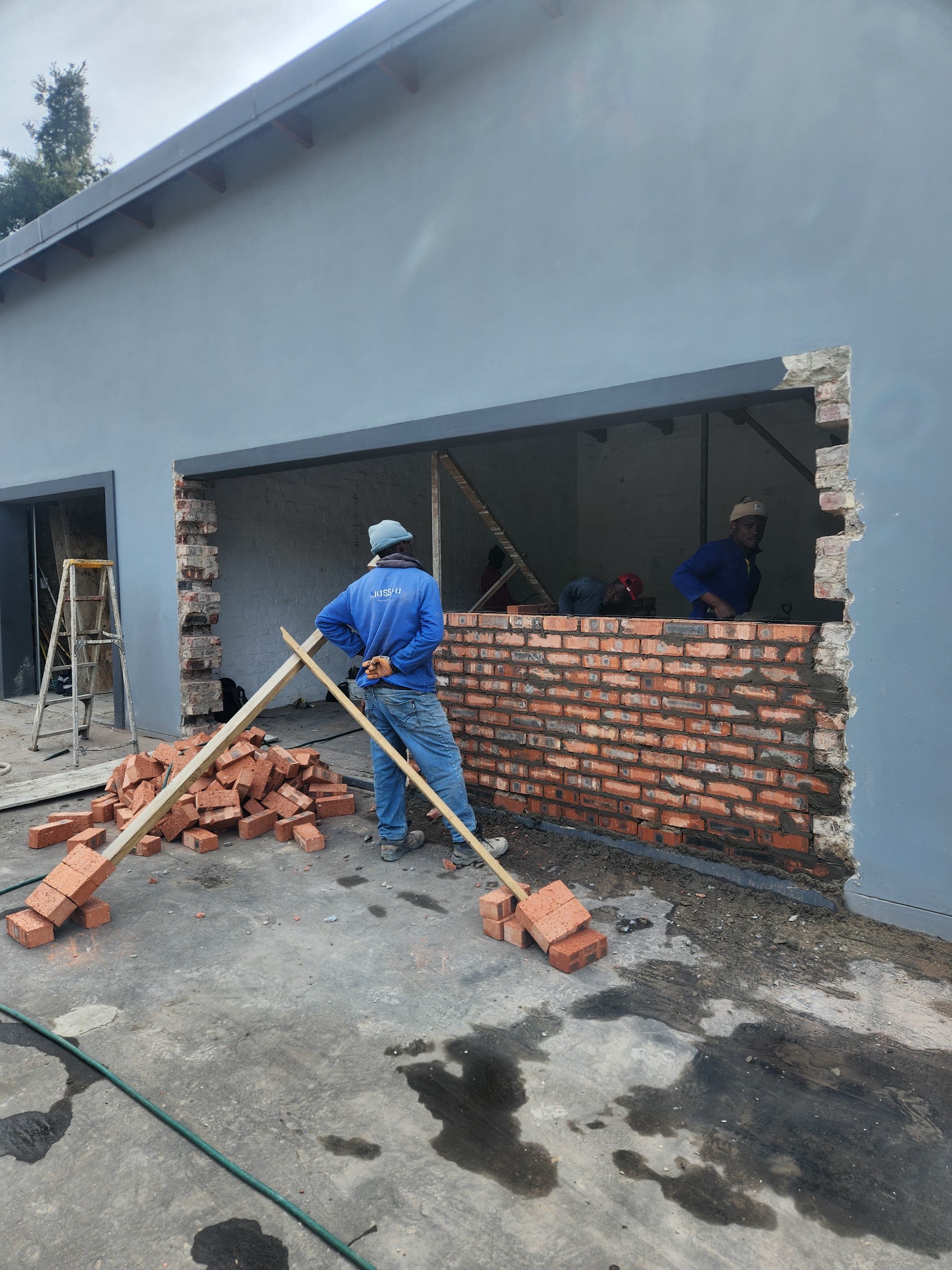 A bricklayer cutting and rebuilding an opening in an existing brick wall