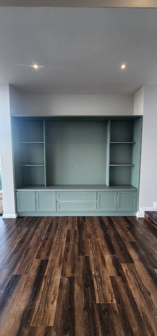 A built-in sage green wall unit with open shelving and cupboards