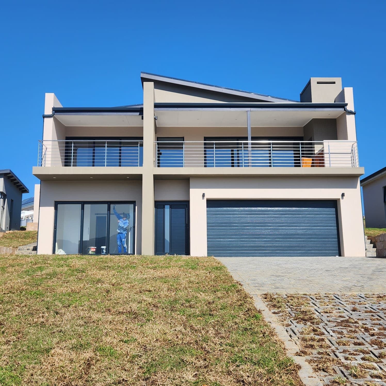 A completed two storey home with a dark garage door, on a grassed slope