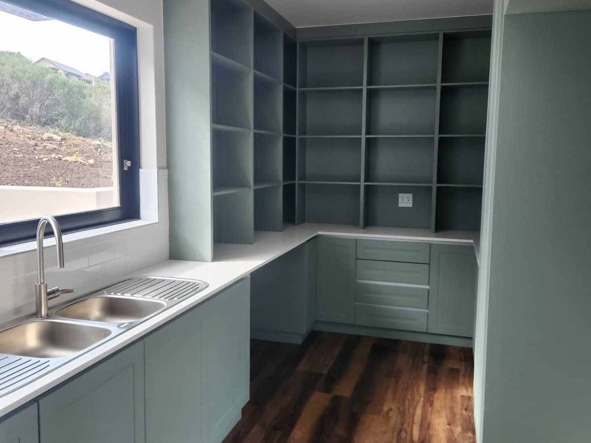 A fitted kitchen in sage green with open shelving and timber floors