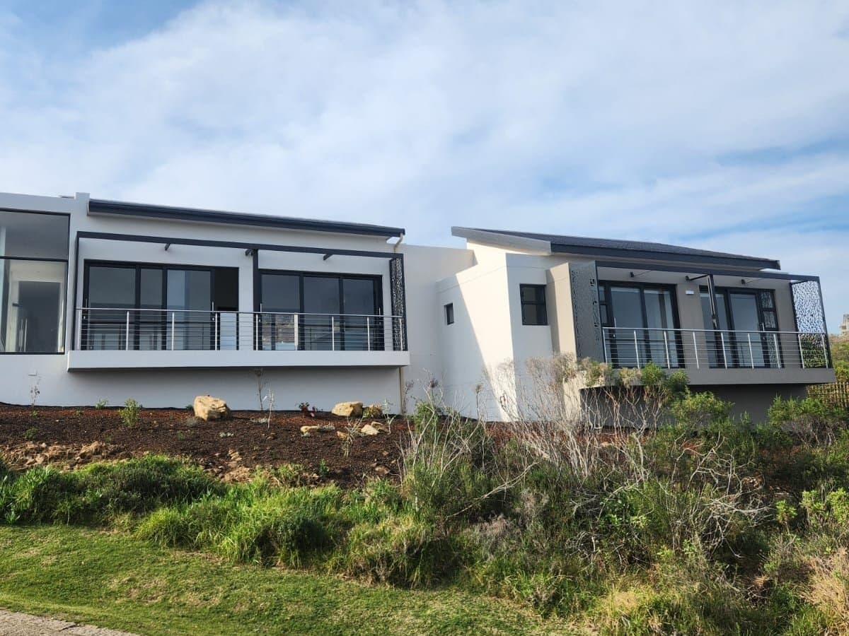 A completed white rendered home with balconies, set on a planted slope